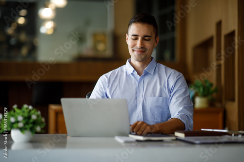 Smiling businessman working on a laptop computer in a modern office,doing finances, accounting analysis, report data pointing graph Freelance education and technology concept.