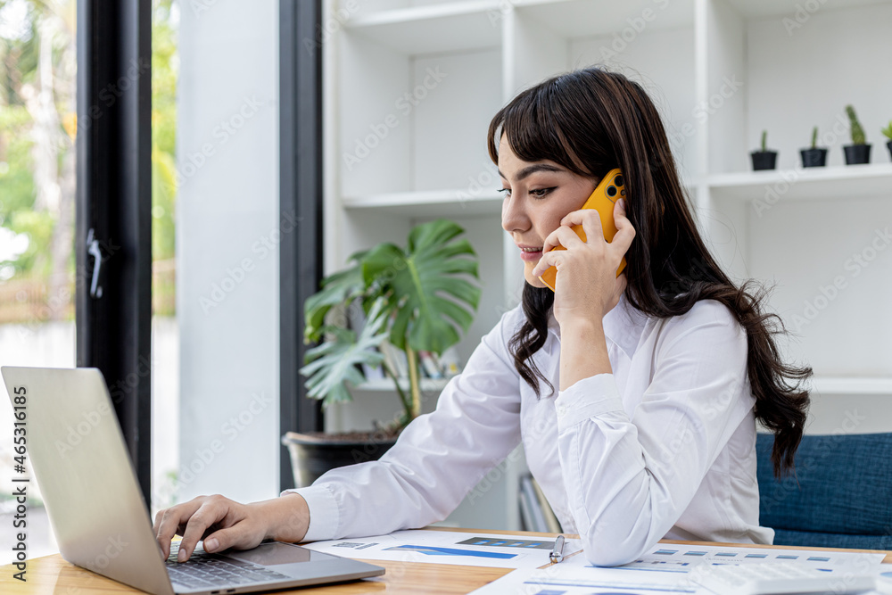 Beautiful Asian businesswoman talking on mobile phone and using laptop, concept image of Asian business woman working smart, modern female executive, startup business woman, business leader woman. Beautiful Asian businesswoman talking on mobile phone and using laptop, concept image of Asian business woman working smart, modern female executive, startup business woman, business leader woman.