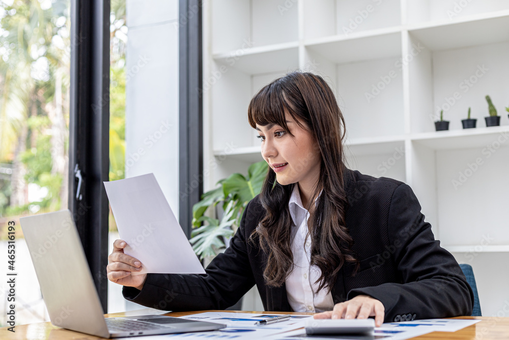 A beautiful Asian businesswoman sitting in her private office, she is checking company financial documents, she is a female executive of a startup company. Concept of financial management.