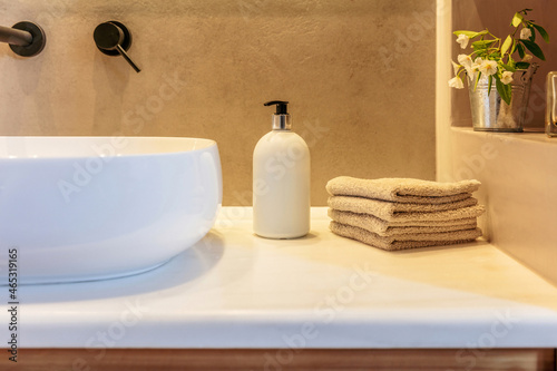 Modern bathroom interior detail. Hand towels folded, soap dispenser and white sink basin on a table