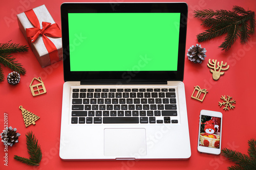 Laptop with green screen, mobile phone and Christmas decorations on red background.Concept: selection gifts, online shopping, Christmas sales, seasonal advertising © Irina Ermakova