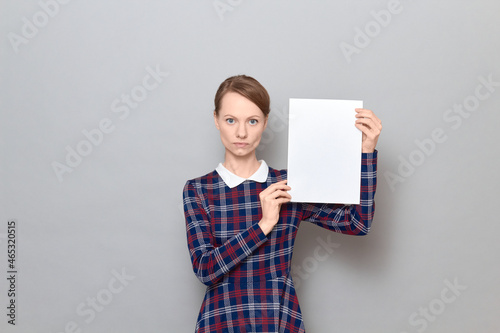 Studio portrait of serious young woman holding white blank paper sheet
