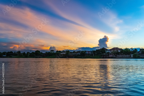 Houses and restaurants on the riverside in the lifestyle of rural Thai society in the evening when the sun shines through the clouds.