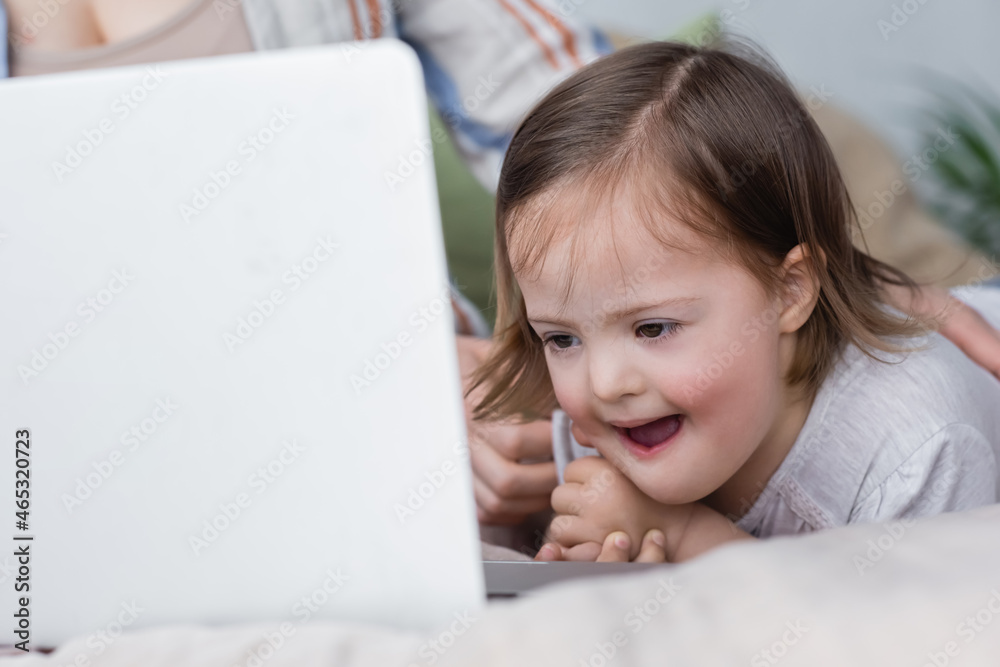 Excited child with down syndrome looking at blurred laptop near mother. Excited child with down syndrome looking at blurred laptop near mother.
