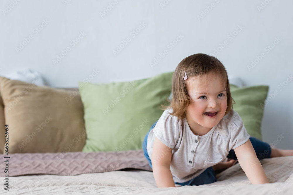 Happy child with down syndrome looking away on bed at home. Happy child with down syndrome looking away on bed at home.