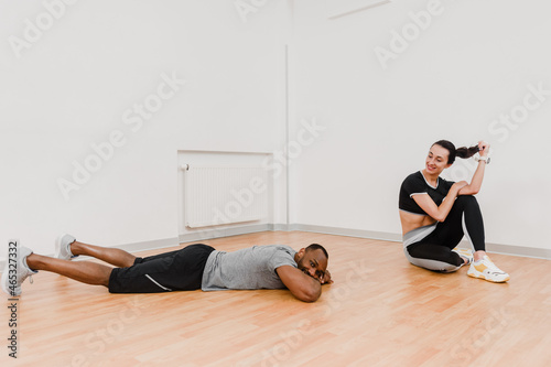 Two athletic man and woman resting after training and lying on floor in gym