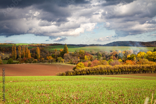 Landschaft im Herbst mit Acker und bunten Bäumen mit  dramatischem Himmel und Rauch eines Feuers.