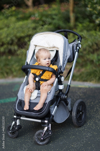 Sweet caucasian baby girl ten months old sitting in stroller outdoors. Little child in pram. Infant kid sits in pushchair. Summer walks with kids. Family leisure with little child. © Алина Бузунова