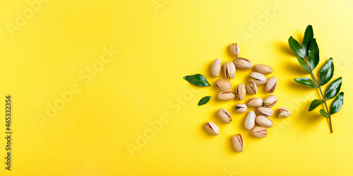Pistachios with leaves on yellow background, top view. Set of pistachio nuts. Copy space