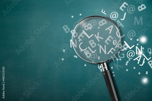A magnifying glass with part of scattered English alphabet letters on the desk background
