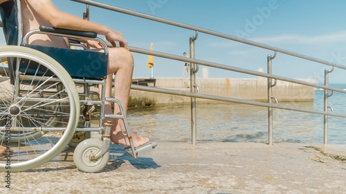 Man with disability on a wheelchair being transported into sea for swimming using a ramp.