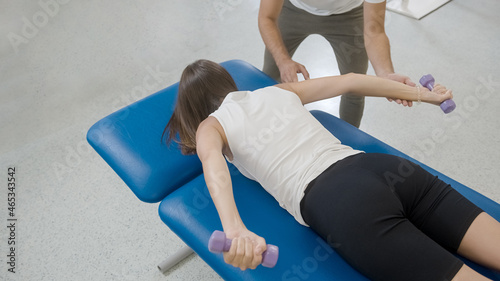 Photos Woman doing shoulder stabilization exercises with small weights, with a help of