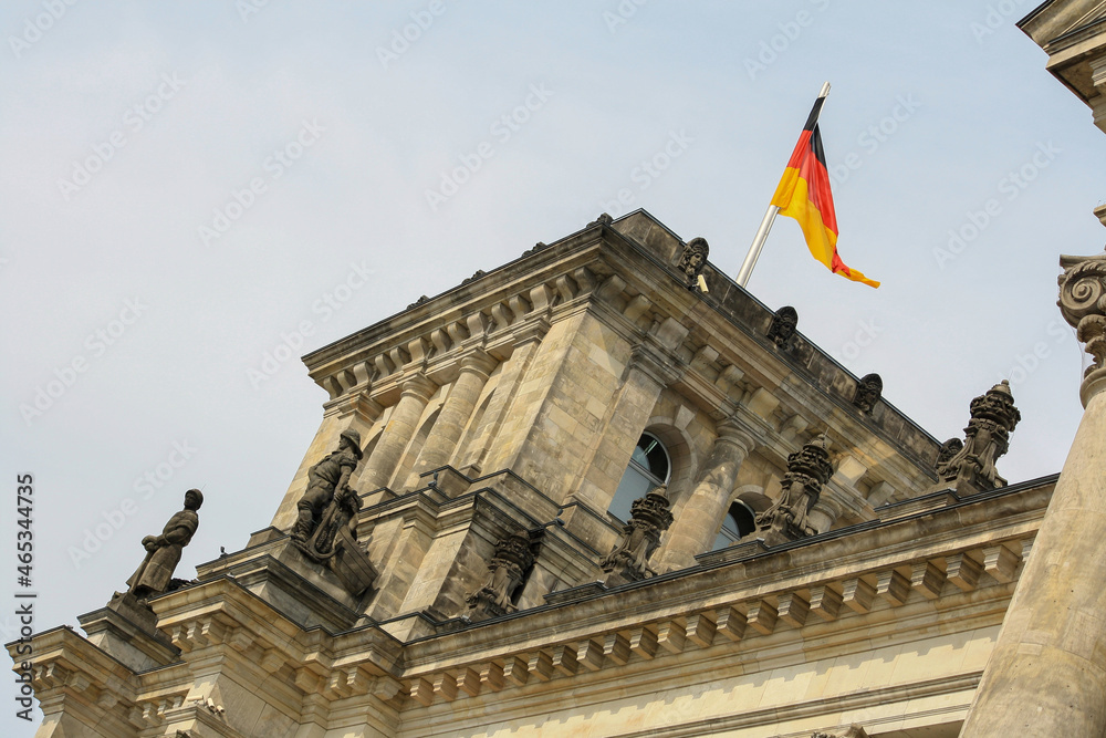 Exterior of Reichstag building in summer with Germany national flag on top and clouds in blue sky background. No people.