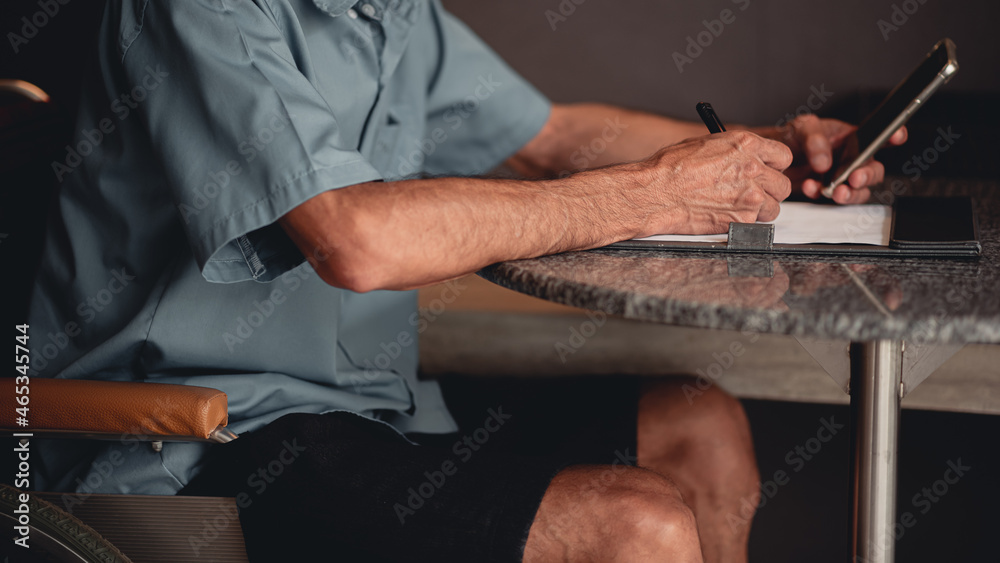 Hands of senior man with disability holding a pen to writing something with business working or sign name on important document by himself on desk in home office, People work and using phone concept.