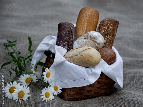 Still life of different types of bread baguettes in a wicker basket and a delicate bouquet of daisies