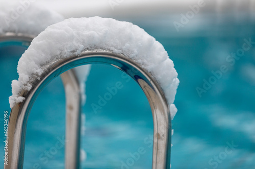 An outdoor swimming pool with blue water/tiles and rails covered with snow