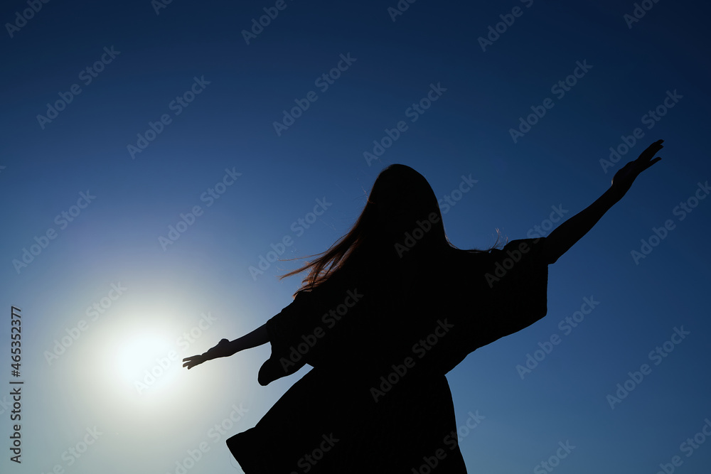 Silhouette dance of beautiful caucasian elegant girl in dress dancing during sunset or woman performing modern dance outdoor in sunny day against blue sky. High quality image