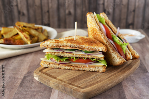 Sandwich with ham, cheese, tomato, onion and salad on wooden board with fries