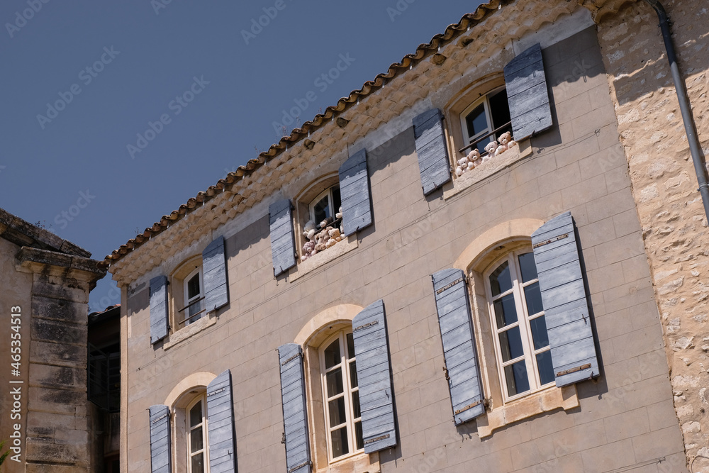 Beige facade of an old house with pale cornflower blue color shutters decorated with bears in the windows. Wooden shutters and sky of the same color. Travel and tourism concept.