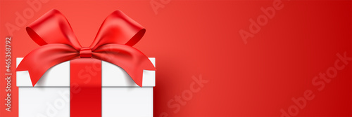 White gift box wrapped with ribbon standing on a red horizontal background with copy space. Realistic giftbox vector banner.