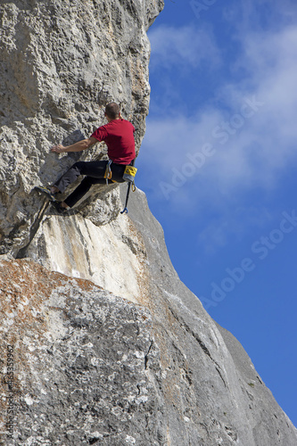 Young sports man climbing natural high rocky wall