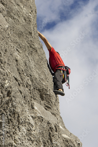 Young sports man climbing natural high rocky wall