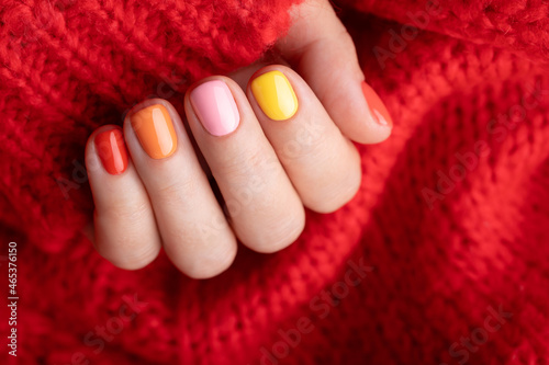 Female hand in red pullover with colorful manicure.