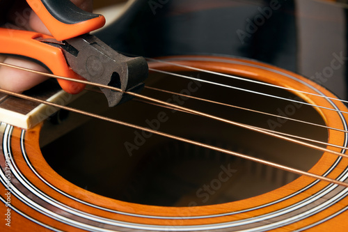 Guitar restring: musician cut strings from an acoustic guitar photo