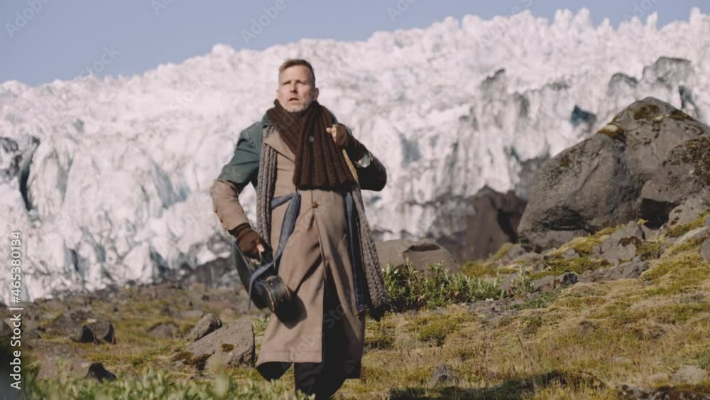 Man In Greatcoat Carrying Guitar Case And Bag Away From Glacier Man In Greatcoat Carrying Guitar Case And Bag Away From Glacier