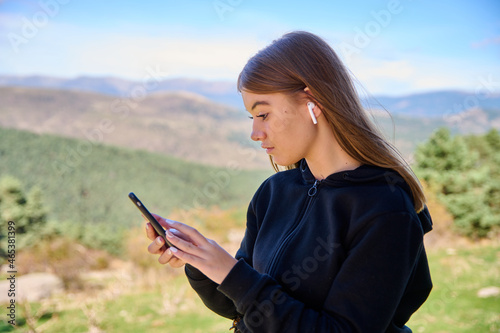 Caucasian lady listening to music and typing on her phone with the green hills on the background