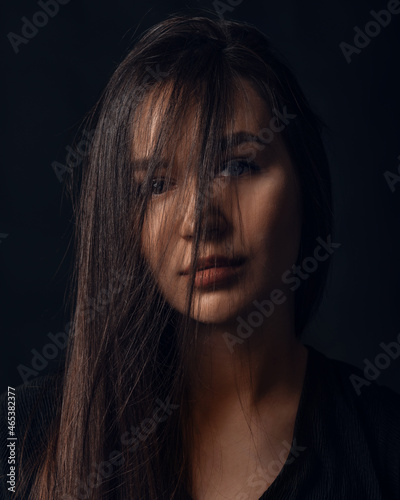 Studio portrait of pretty brunette woman with hair on the face on black background.