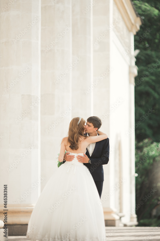 Lovely happy wedding couple, bride with long white dress posing in beautiful city Lovely happy wedding couple, bride with long white dress posing in beautiful city