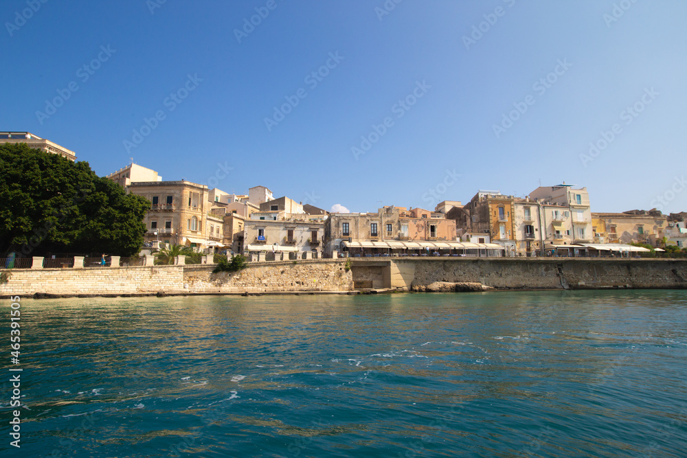 Sea side view of Siracusa Ortigia island old town buildings houses and churches in sunny summer day. A bright colorful photo good for touristic booklet or book, boat trip ads, posters etc.