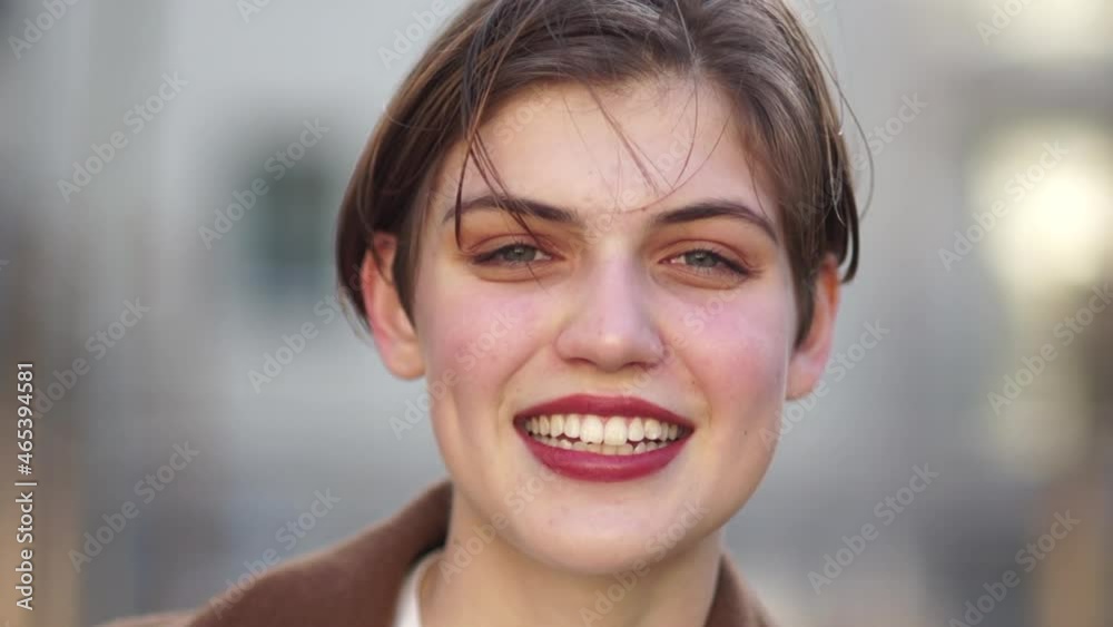 Close portrait of a lovely short-haired young woman. The girl smiles and straightens her hair. Red lipstick, white-toothed smile Close portrait of a lovely short-haired young woman. The girl smiles and straightens her hair. Red lipstick, white-toothed smile