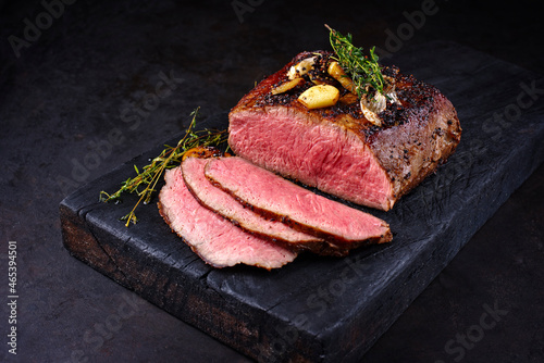 Traditional Commonwealth Sunday roast with sliced cold cuts roast beef with garlic and salt as close-up on a rustic charred wooden board photo