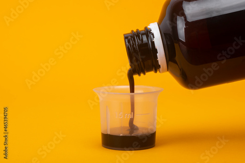 The cough syrup is poured into a measuring glass.