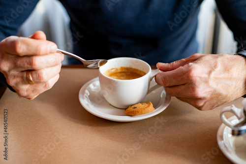 Hand puts a sugar cube in the coffee cup.A man's hand uses a cutlery to take a lump of sugar to add to black coffee.