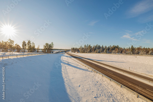 Beautiful landscape view on cold sunny day. Snowy road merging with cloudless blue sky. Sweden. 