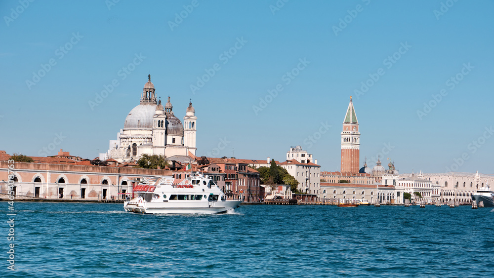 Central Venice, view from lagoon. City skyline with Punta della Dogana, church Santa Maria della Salute, Doge's palace and St Mark's Campanile tower. Modern yacht ship goes along the Venetian Lagoon