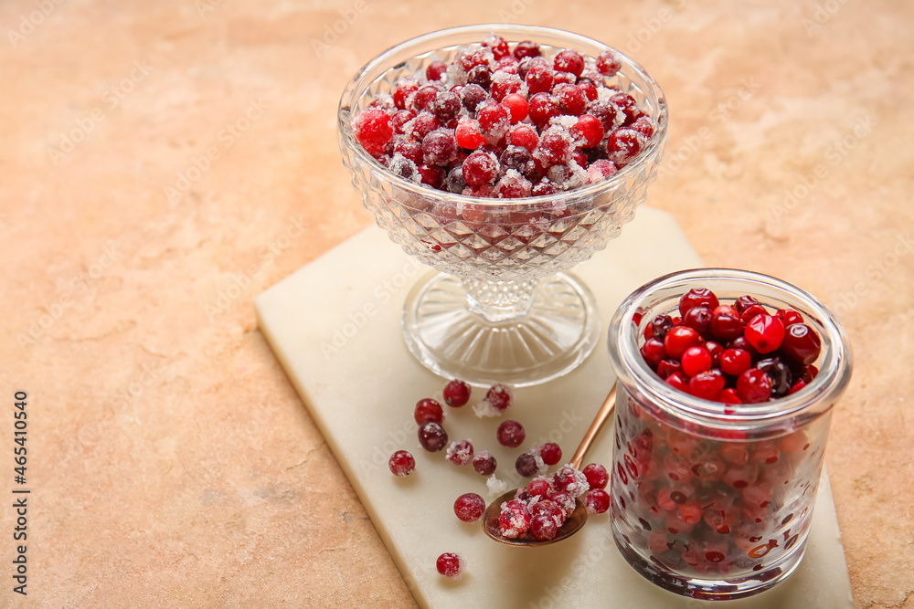 Glass bowl and jar with tasty sugared cranberries on beige background Glass bowl and jar with tasty sugared cranberries on beige background