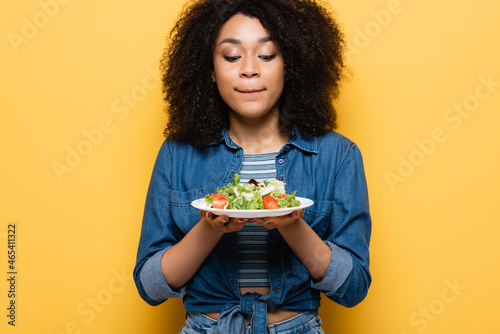 african american woman holding plate with tasty vegetable salad on yellow