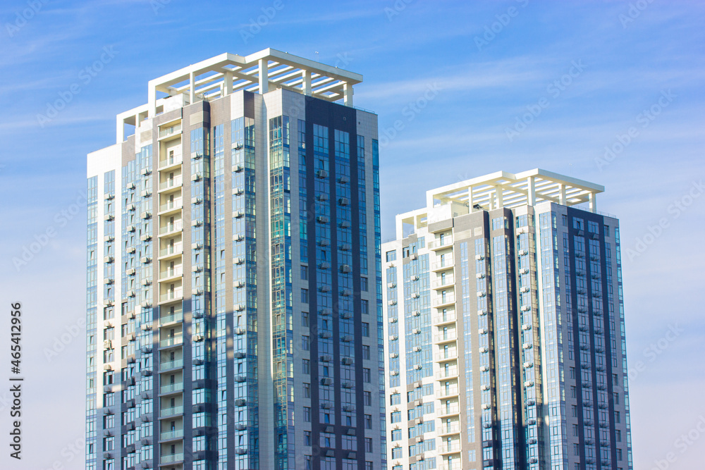 Two modern tall apartment buildings against a blue sky at sunny day. The building with symmetrical modern architecture in big city. Condominium. Real estate investing, buying, renting. Business center