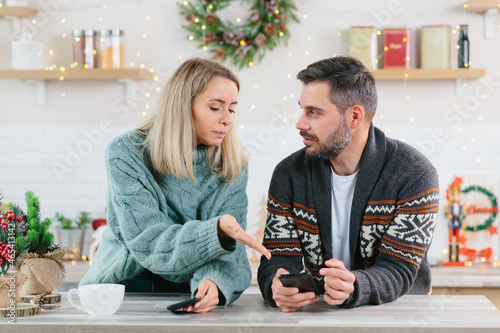 Young family couple quarreled over mobile phone and social networks, man and woman sad during the New Year holidays and Christmas photo