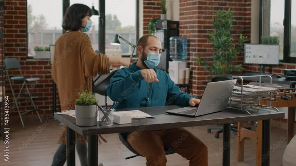 Workmates doing fist bump before work in startup office. Colleagues wearing face masks and working on business project and strategy planning with laptop during coronavirus pandemic. Workmates doing fist bump before work in startup office. Colleagues wearing face masks and working on business project and strategy planning with laptop during coronavirus pandemic.