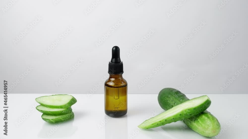 A woman's hand takes from the table, puts on the table a glass dark brown bottle with serum on a white background with cucumber slices A woman's hand takes from the table, puts on the table a glass dark brown bottle with serum on a white background with cucumber slices