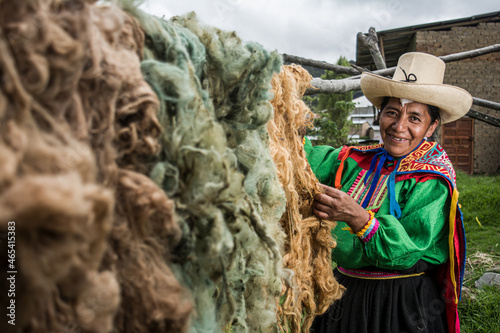 Mujer latinoamericana andina colgando lana de oveja teñida de colores en el campo para secarla en Cañaris Perú photo