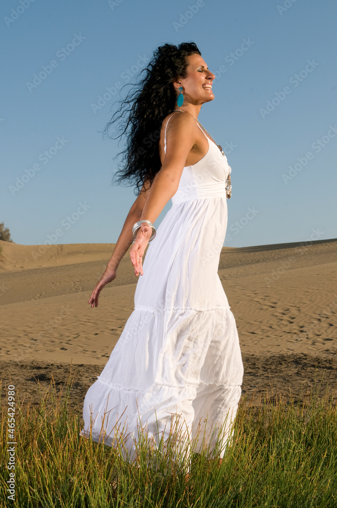 woman on sand enjoying spring or summer sun dressed in white clothes