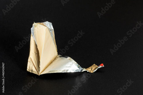 Foil wrapped processed soft cheese slice on a black background. Small triangular piece of portioned cream cheese in a golden aluminium foil. Tasty sandwich ingredient.