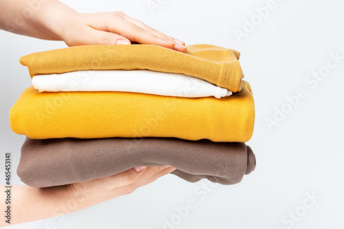 Female hands hold stack of knitted clothes on white background close-up.