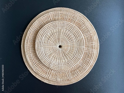 Round shape woven rattan placemat on black background, handmade kitchenware, weave craft product 